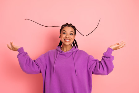 Smiling young female wearing a purple hoodie against a vibrant pink background, cheerfully making a...