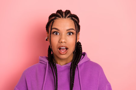Portrait of Young Woman with Braids in Purple Hoodie on Pink Background Expressing Shock and Amazementの写真素材