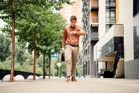 Confident young businessman checking time while walking through modern urban city street with professional demeanorの写真素材