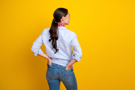 Brunette woman in stylish casual outfit posing on vibrant yellow background in a relaxed manner showcasing fashion and eleganceの写真素材