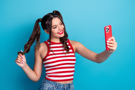 Stylish young woman using smartphone for a selfie in trendy casual wear with striped top, vibrant backgroundの写真素材