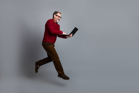 Confident Senior Professional with Laptop in Casual Attire on a Gray Background Displaying Business Presence and Styleの写真素材