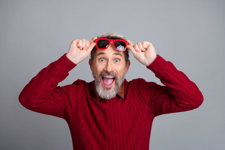 Excited mature man promoting a positive lifestyle with glasses and a casual sweater on a gray backdropの写真素材