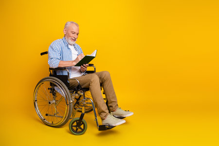 Grandpa in a wheelchair reads a bright yellow studio journal turning rehab into a joyful learning adventure for every dayの写真素材