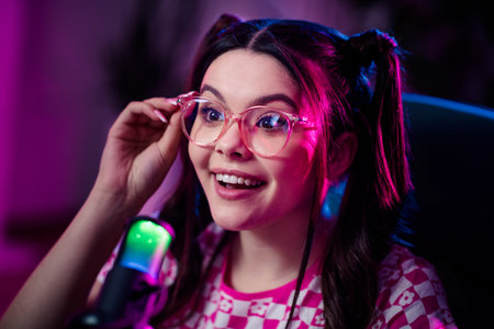 Cheerful female streamer interacting online using a microphone in neon light ambiance, embodying social media creativityの写真素材