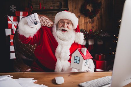 Funny santa at his desk shows off a little house key and a cozy christmas workshop vibe at home for holiday joy and celebrationの写真素材