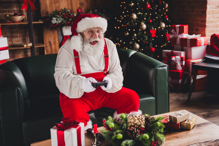 Funny Santa relaxing on a cozy couch among Christmas gifts and a sparkling tree at homeの写真素材
