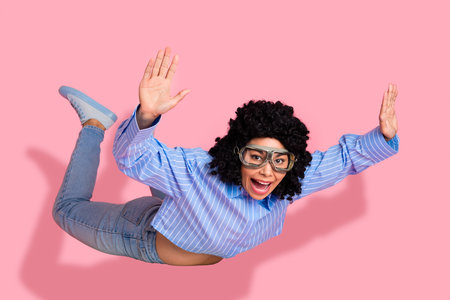 Cheerful woman with curly hair posing joyfully on a pink background wearing a casual outfit and expressive gogglesの写真素材