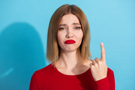 Lovely young female expressing emotion in a red shirt against a vibrant blue background, showcasing modern fashionの写真素材