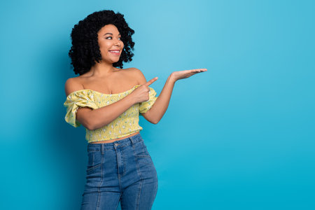 Charming young woman wearing a stylish outfit gesturing joyfully with an open hand against a vibrant blue backgroundの写真素材