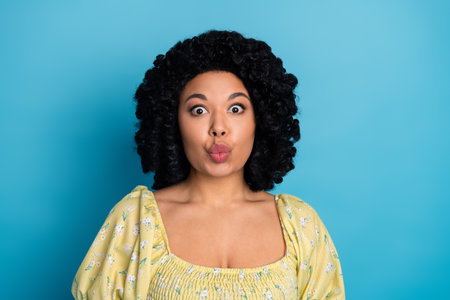 Smiling young woman with curly hair making a funny face against a vibrant blue backgroundの写真素材