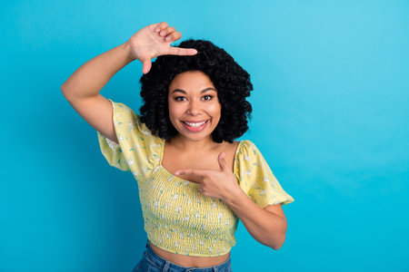 Funny woman with curly hair smiling and gesturing on blue background, showcasing positive emotion...