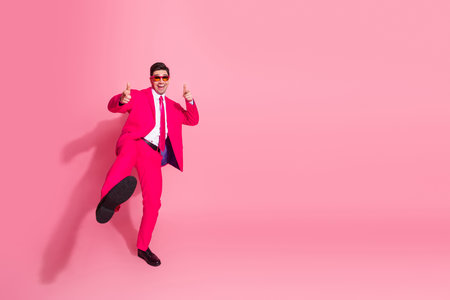 Energetic young man in a vibrant pink suit pointing enthusiastically with a fashionable backgroundの写真素材