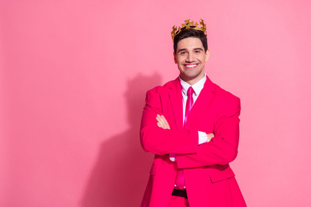 Charming young man in a pink suit and crown posing confidently against a vibrant backdrop, exuding elegance and style.の写真素材