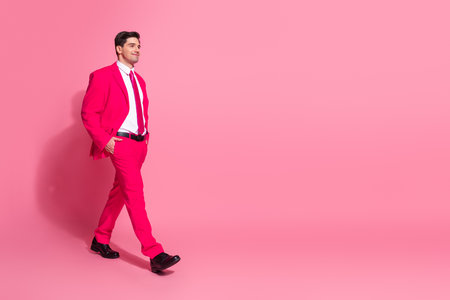 Young man in a vibrant pink suit posing confidently with a dynamic stride on a bold pink backgroundの写真素材
