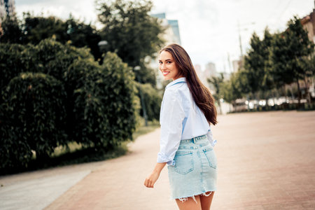 Lovely woman with long brunette hair smiling outdoors in casual clothing on a city street during a leisure strollの写真素材