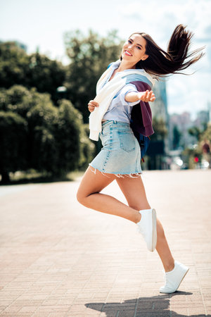 Beautiful brunette woman enjoying a sunny urban day outdoors, showcasing casual fashion in a stylish outfitの写真素材