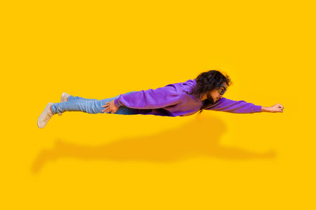 Funky man in purple hoodie acting as if flying against bright yellow background for creative and fun conceptの写真素材