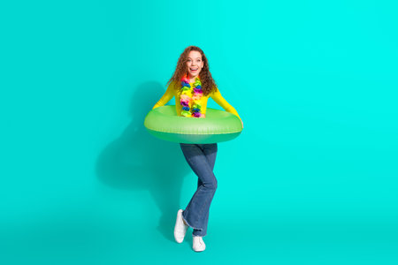 Smiling young woman holding an inflatable ring in a tropical theme with a vibrant teal backgroundの写真素材