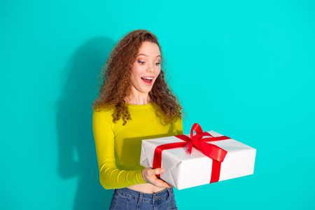 Smiling young girl receives wrapped gift with excitement against vibrant turquoise background...