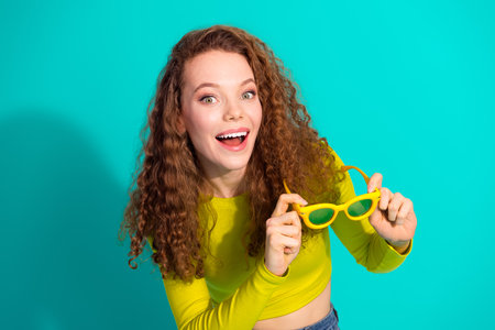 Young girl posing with vibrant yellow sunglasses against a turquoise background, expressing joy and style in a casualの写真素材