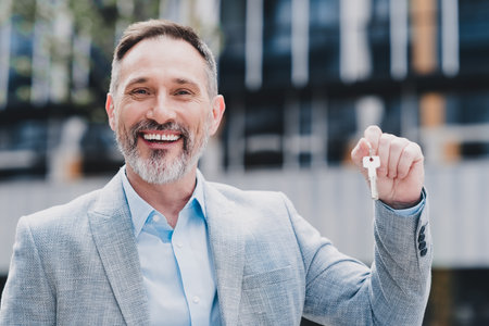 Confident business professional in modern city smiling while holding keys in sleek blazer for urban real estate successの写真素材