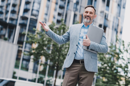 Confident businessman on a busy city street outside a modern office building with a tablet and a smileの写真素材