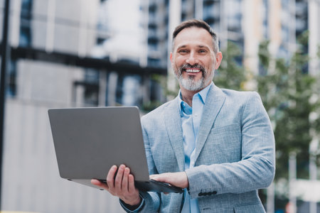 Professional businessman smiling in a modern city holding a laptop ready for urban business and real estate work in a stylish corporate settingの写真素材