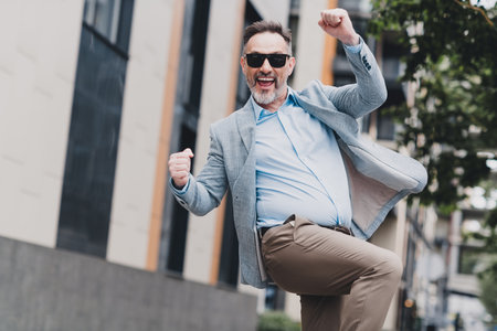 Energetic mature businessman jumps with confidence in a stylish suit through a modern city street conveying success professionalism and urban momentumの写真素材