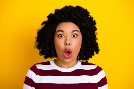 Surprised young woman in striped sweater against a vibrant yellow background, showcasing expressive emotionの写真素材