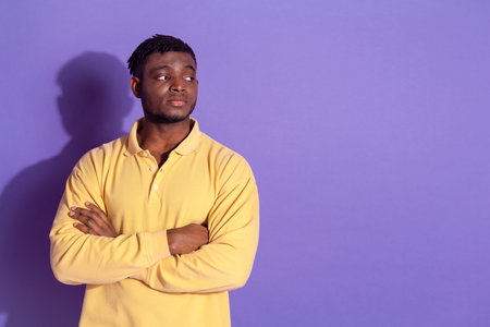 Photo portrait of pretty young man look empty space crossed hands strict face wear trendy yellow outfit isolated on purple color backgroundの写真素材