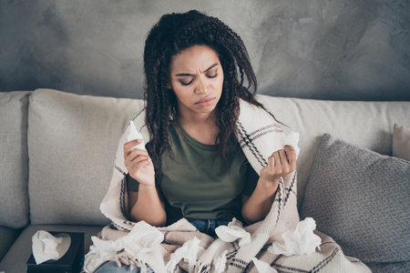 Photo of unhappy upset woman covering blanket having running nose indoors house apartment roomの写真素材