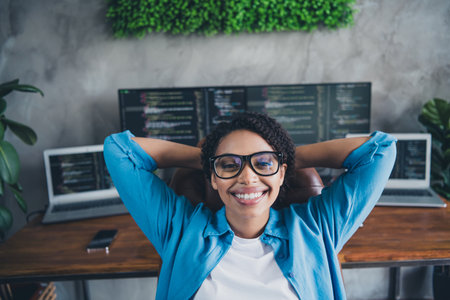 Photo of young lady sit armchair finish work hands behind head dressed blue shirt comfortable programmer startup office loft room interiorの写真素材
