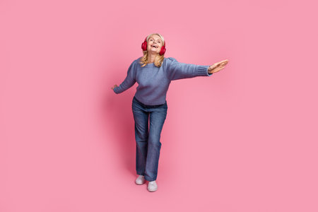 Full length photo of lovely pensioner lady have fun headphones dance dressed stylish blue knitted garment isolated on pink color backgroundの写真素材