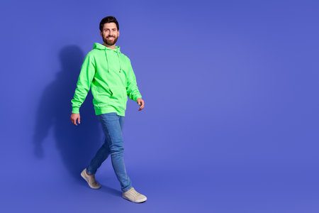 Full size photo of pretty young male walking empty space wear trendy green outfit isolated on purple color backgroundの写真素材