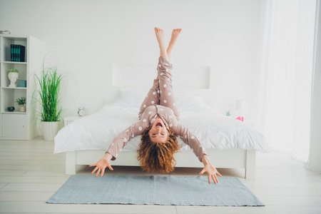Young woman with red hair joyfully stretches on bed in cozy bedroomの写真素材