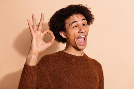 Young man giving an enthusiastic okay sign in casual outfit on beige backgroundの写真素材