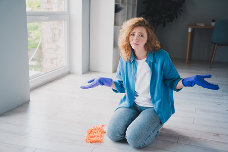 Full length photo of lovely young ginger girl tired wipe floor depressed confused dressed blue garment spacious house indoors roomの写真素材