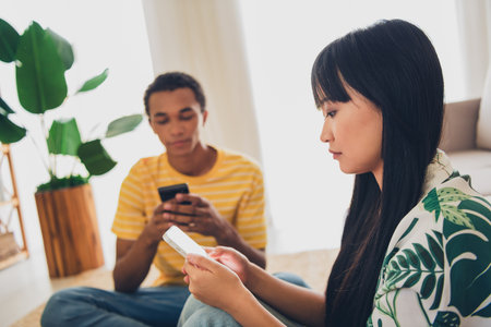 Photo of cute young couple wife husband sitting separate chatting typing writing social media post indoors flat apartmentの写真素材
