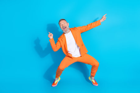 Full size photo of trendy modern aged man dance point fingers wear orange costume isolated on blue color backgroundの写真素材
