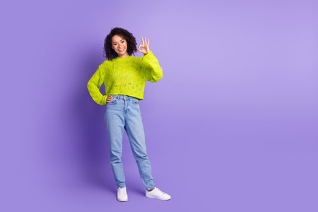 Photo of curly haired student girl in green trendy knitted sweater positive demonstrate peace symbol isolated on violet color backgroundの写真素材
