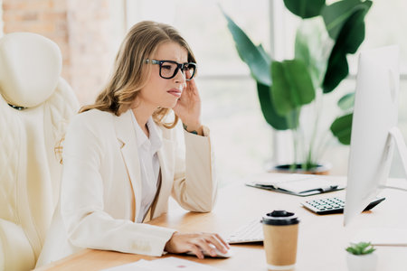 Young professional businesswoman in formalwear working in a modern office setting while focused on her computer tasksの写真素材