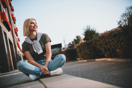 Full size photo of young blonde girl sit concrete border wear khaki outfit tied shoulders sweater walk park sunny spring weatherの写真素材
