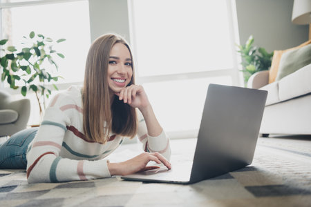 Young woman enjoying a leisure weekend at home relaxing with her laptop in a cozy living room setting under natural daylightの写真素材