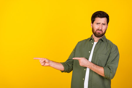 Portrait of young man indicating fingers empty space on yellow backgroundの写真素材