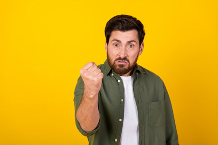 Photo of young man raising fist, wearing khaki shirt isolated on yellow backgroundの写真素材