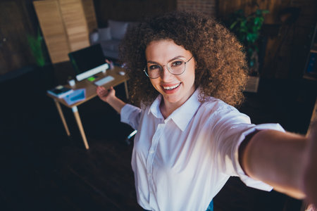 Photo of lovely curly young lady take selfie photo hand point dressed formalwear business manager comfortable startup office room interiorの写真素材