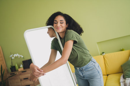 Photo of attractive young woman cheerful hugging mirror dressed green outfit daylight home interior living roomの写真素材