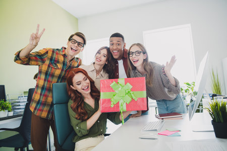 Photo of smiling happy web designers showing v-sing giving present box new collegue indoors workplace workstationの写真素材