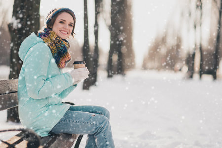 Profile side photo of attractive cheerful young woman sit bench cold snow weather smile drink coffee outdoors outsideの写真素材